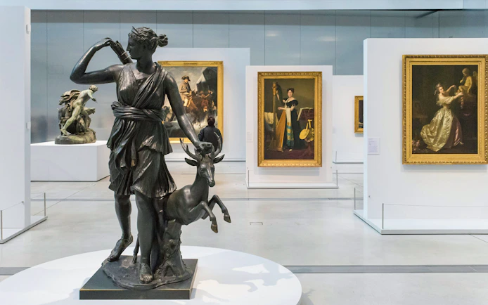 Sculpture of Diana with deer in Louvre Museum gallery, surrounded by classic paintings.