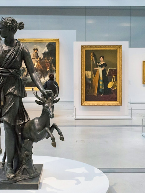Sculpture of Diana with deer in Louvre Museum gallery, surrounded by classic paintings.