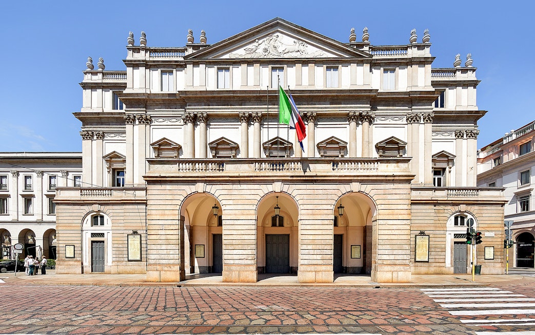 La Scala Theatre facade in Milan, Italy, with Italian flag displayed.