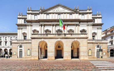La Scala Theatre facade in Milan, Italy, with Italian flag displayed.