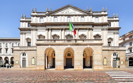 La Scala Theatre facade in Milan, Italy, with Italian flag displayed.