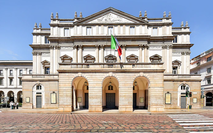 La Scala Theatre facade in Milan, Italy, with Italian flag displayed.