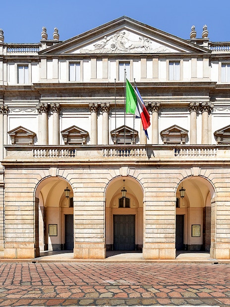 La Scala Theatre facade in Milan, Italy, with Italian flag displayed.