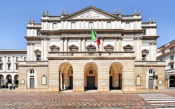 La Scala Theatre facade in Milan, Italy, with Italian flag displayed.
