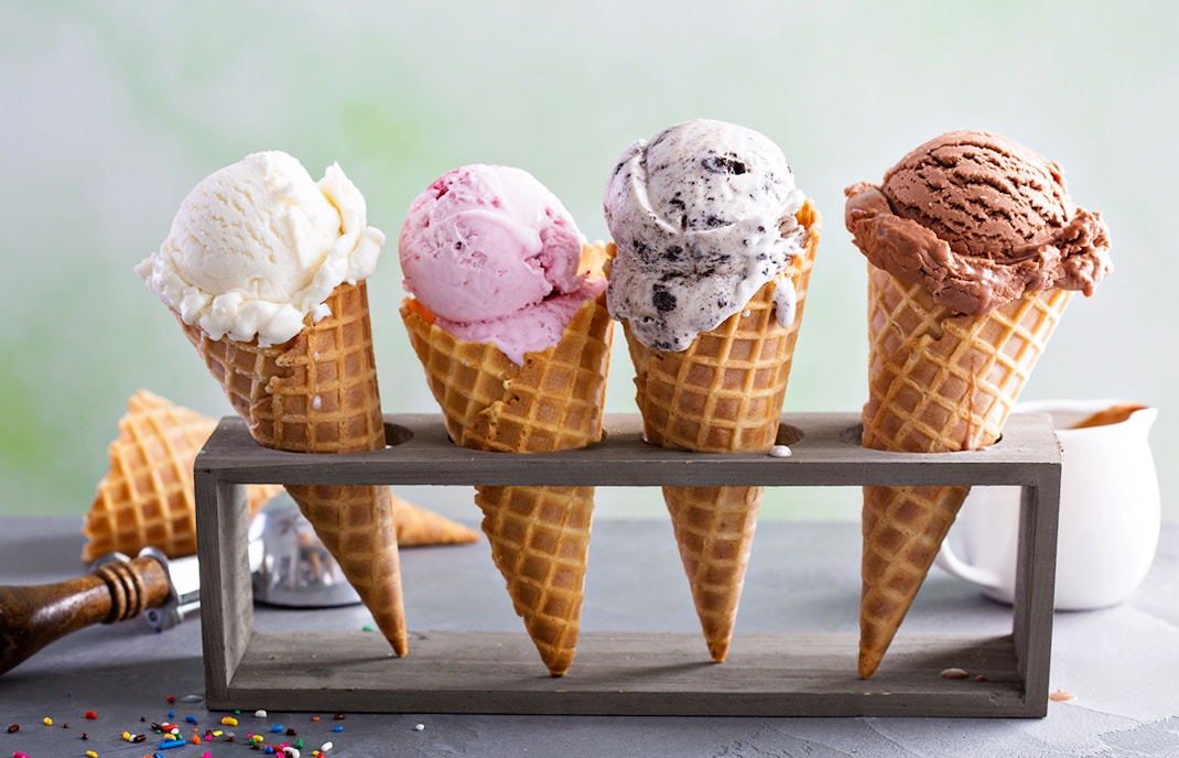 Four ice cream cones with different flavors on a wooden stand.
