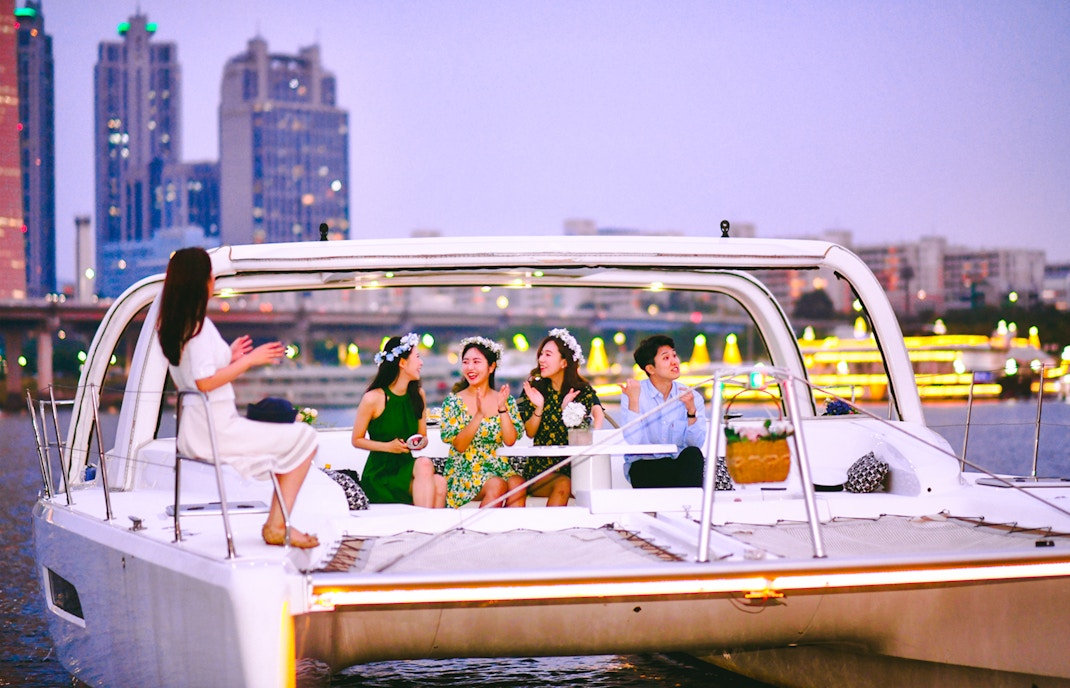 People enjoying a yacht cruise on the Han River in Seoul with city skyline in the background.