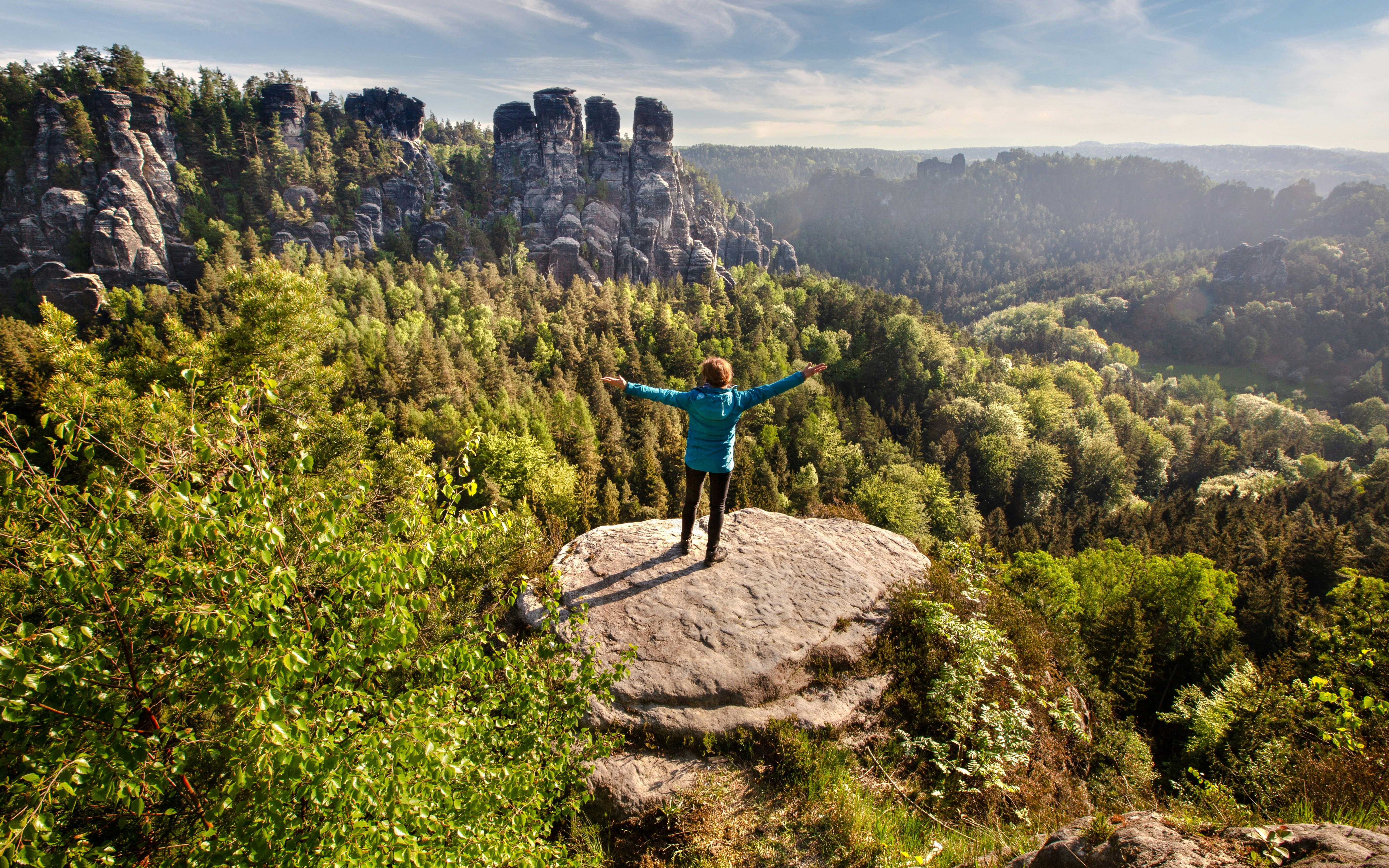 Hiker on rock overlooking forested cliffs in Saxon & Bohemian Switzerland.