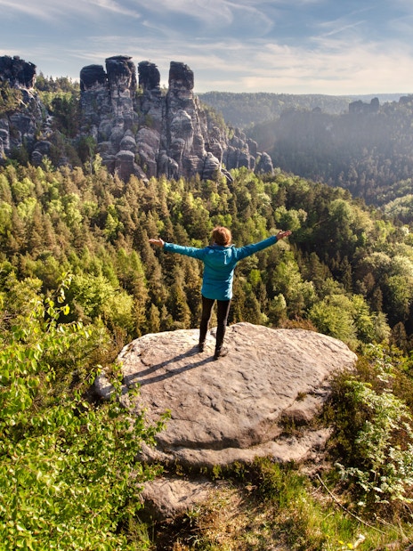 Hiker on rock overlooking forested cliffs in Saxon & Bohemian Switzerland.