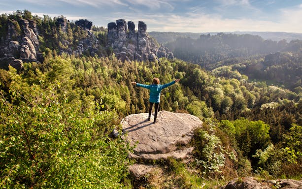 Hiker on rock overlooking forested cliffs in Saxon & Bohemian Switzerland.