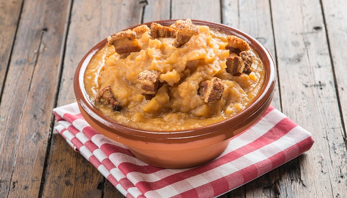Patatas revolconas with crispy pork in a clay bowl on a wooden table.