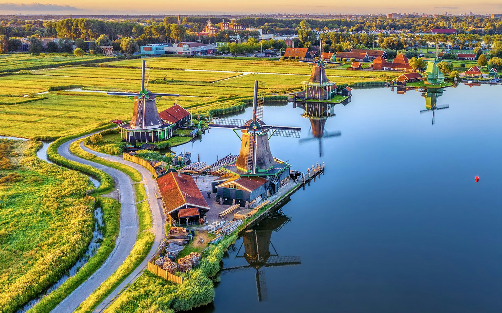 Zaanse Schans windmills by a river with green fields in the Netherlands.