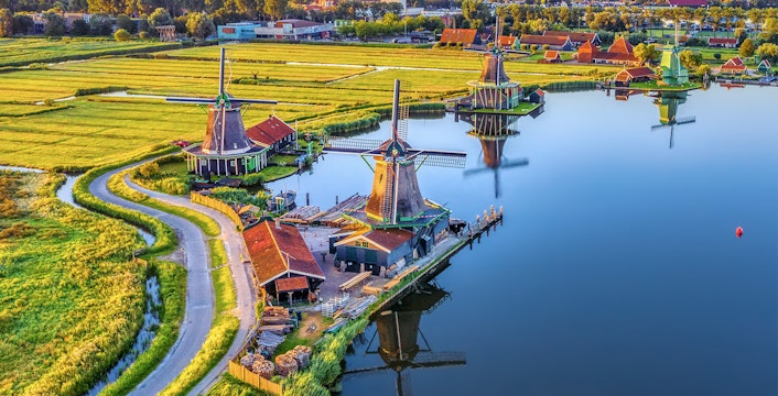 Zaanse Schans windmills by a river with green fields in the Netherlands.