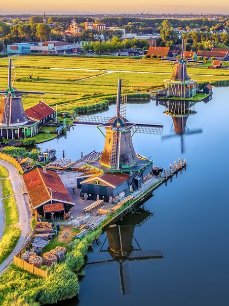 Zaanse Schans windmills by a river with green fields in the Netherlands.