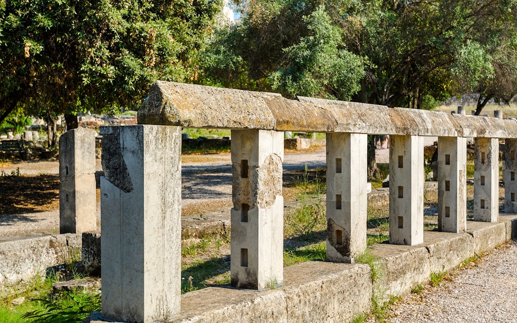 Monument of the Eponymous Heroes in Ancient Agora, Athens, with stone structure and trees.
