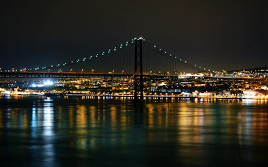 Lisbon's Ponte 25 de Abril bridge illuminated at night over the Tagus River.