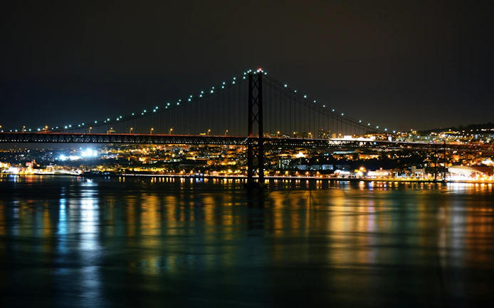 Lisbon's Ponte 25 de Abril bridge illuminated at night over the Tagus River.