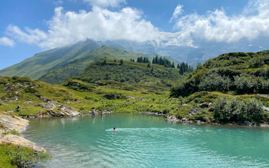 People swimming in a turquoise lake surrounded by green hills at Trübsee, Switzerland, during a summer tour from Lucerne.