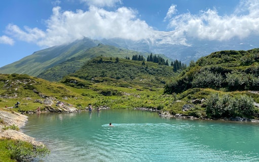 People swimming in a turquoise lake surrounded by green hills at Trübsee, Switzerland, during a summer tour from Lucerne.
