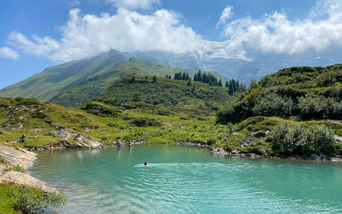 People swimming in a turquoise lake surrounded by green hills at Trübsee, Switzerland, during a summer tour from Lucerne.