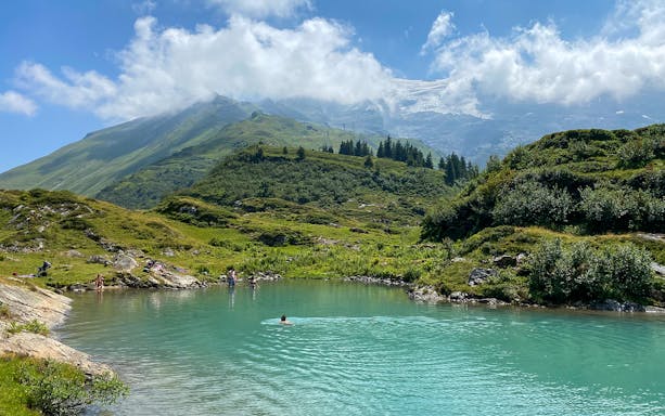 People swimming in a turquoise lake surrounded by green hills at Trübsee, Switzerland, during a summer tour from Lucerne.