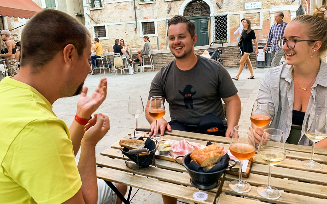 People enjoying a guided food tour in Venice, sharing local dishes and wine at an outdoor cafe.