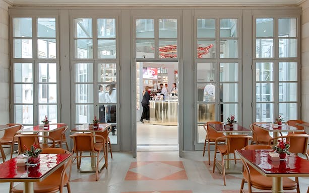 Elegant indoor seating area with red tables and chairs, overlooking a bar in Venice's Royal Garden.