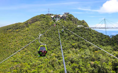SkyCab cable car ascending over lush hills in Langkawi, with Sky Bridge in the background.