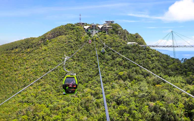 SkyCab cable car ascending over lush hills in Langkawi, with Sky Bridge in the background.
