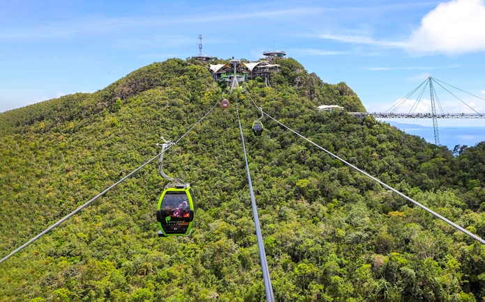 SkyCab cable car ascending over lush hills in Langkawi, with Sky Bridge in the background.
