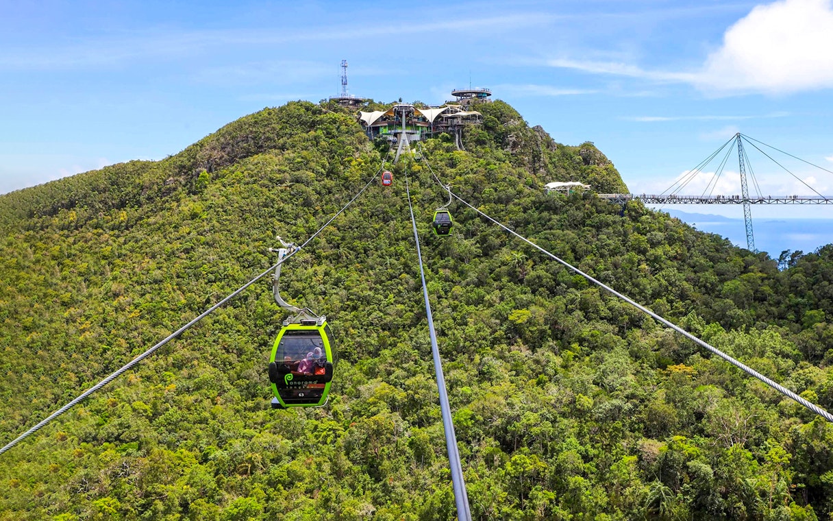 SkyCab cable car ascending over lush hills in Langkawi, with Sky Bridge in the background.