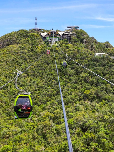 SkyCab cable car ascending over lush hills in Langkawi, with Sky Bridge in the background.