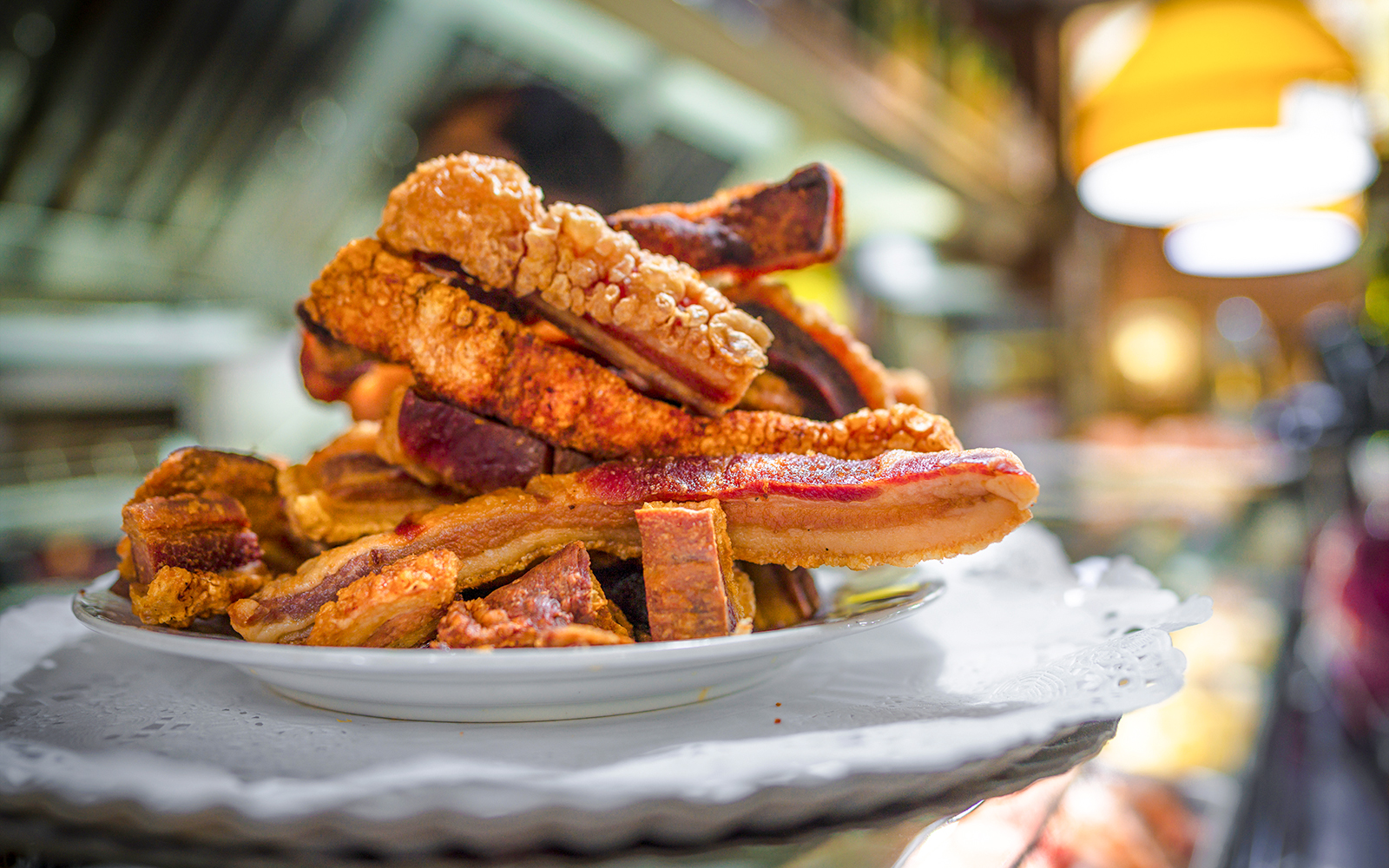 Torreznos pork belly slices stacked on a white plate in a restaurant setting.