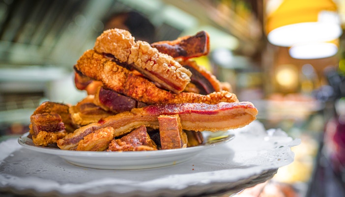 Torreznos pork belly slices stacked on a white plate in a restaurant setting.
