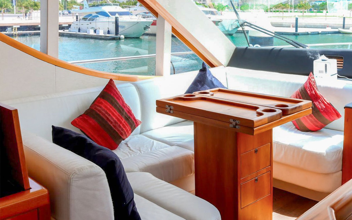 Luxury yacht interior with plush seating and table, Dubai Marina in background.