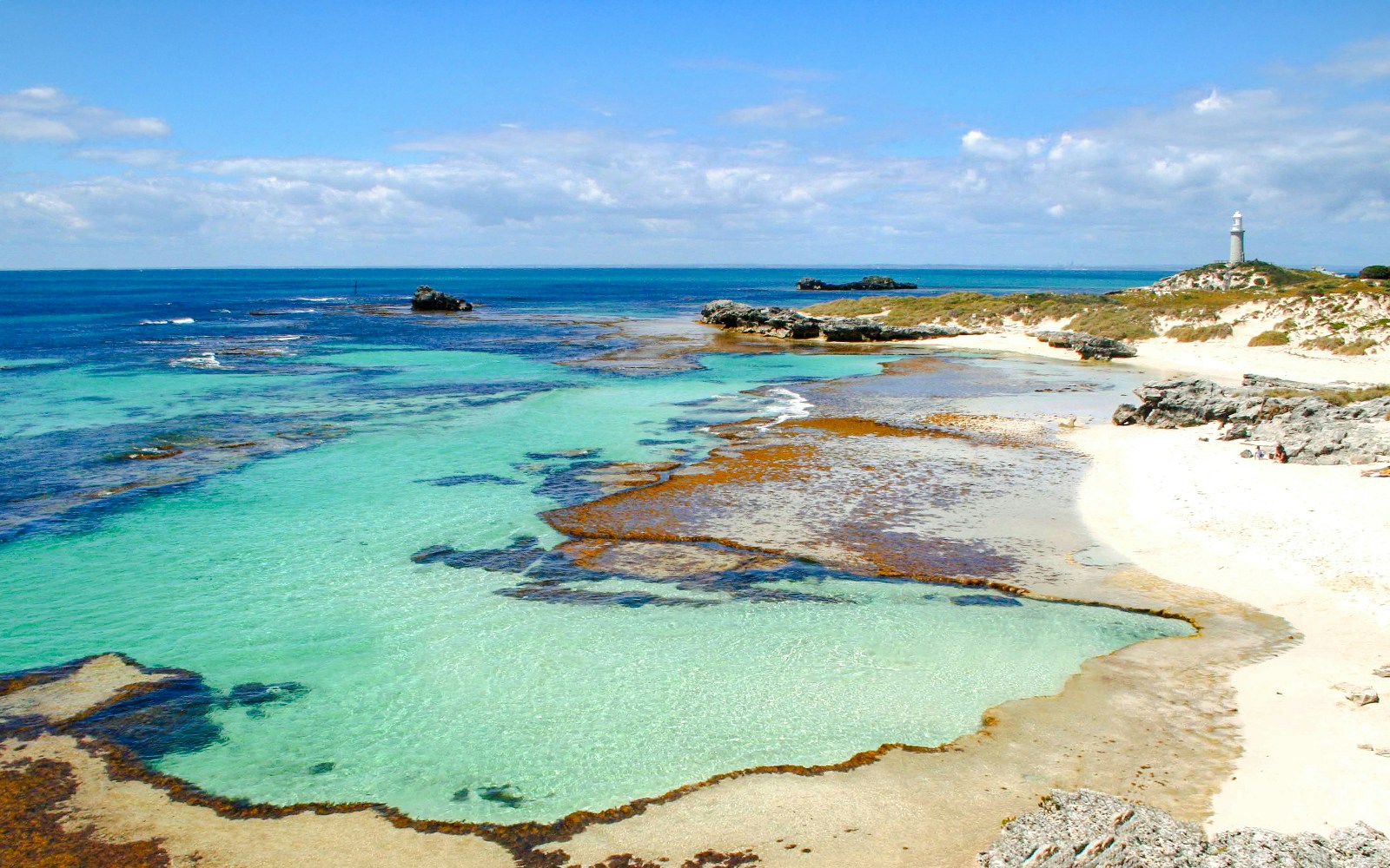 Clear waters and rocky shoreline at The Basin, Rottnest Island with a distant lighthouse.
