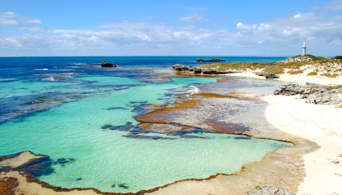 Clear waters and rocky shoreline at The Basin, Rottnest Island with a distant lighthouse.