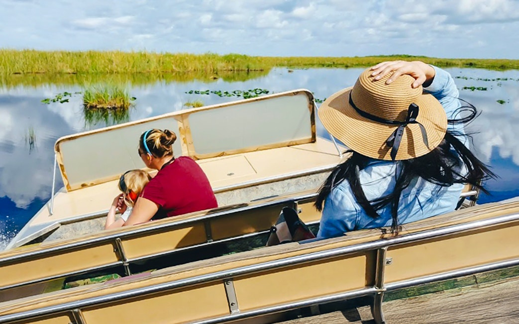 Guests on airboat ride through Everglades wetlands, Florida, surrounded by lush vegetation.