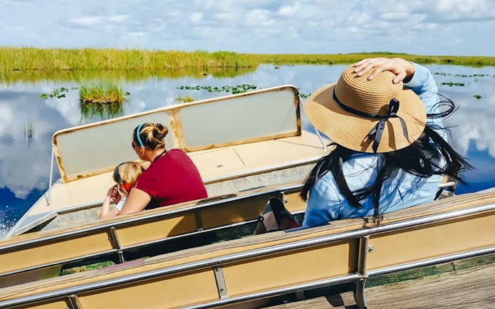 Guests on airboat ride through Everglades wetlands, Florida, surrounded by lush vegetation.