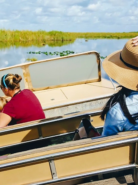 Guests on airboat ride through Everglades wetlands, Florida, surrounded by lush vegetation.
