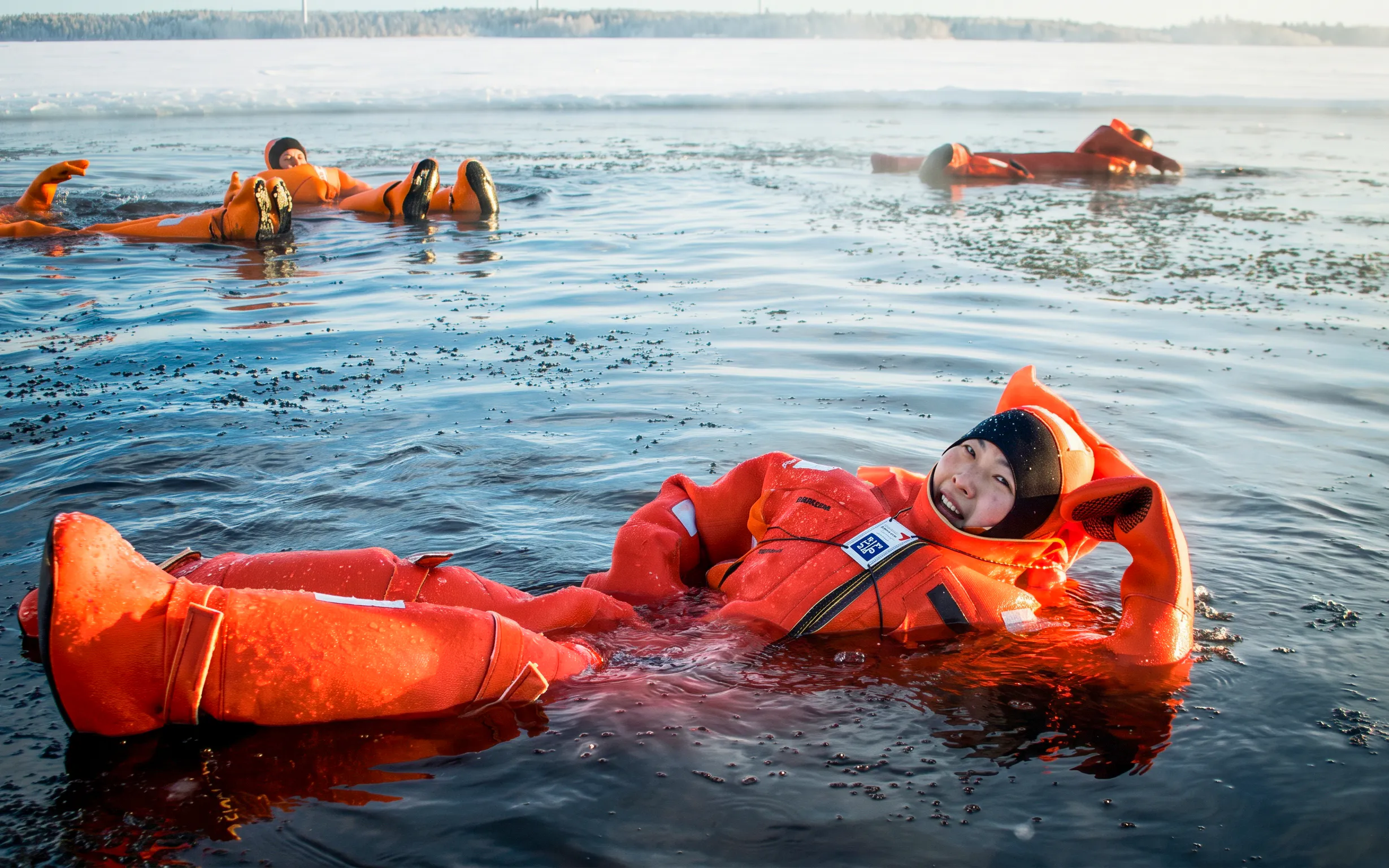 Participants in orange suits floating in icy water during an Icebreaker Cruise in Rovaniemi.