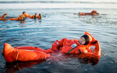 Participants in orange suits floating in icy water during an Icebreaker Cruise in Rovaniemi.