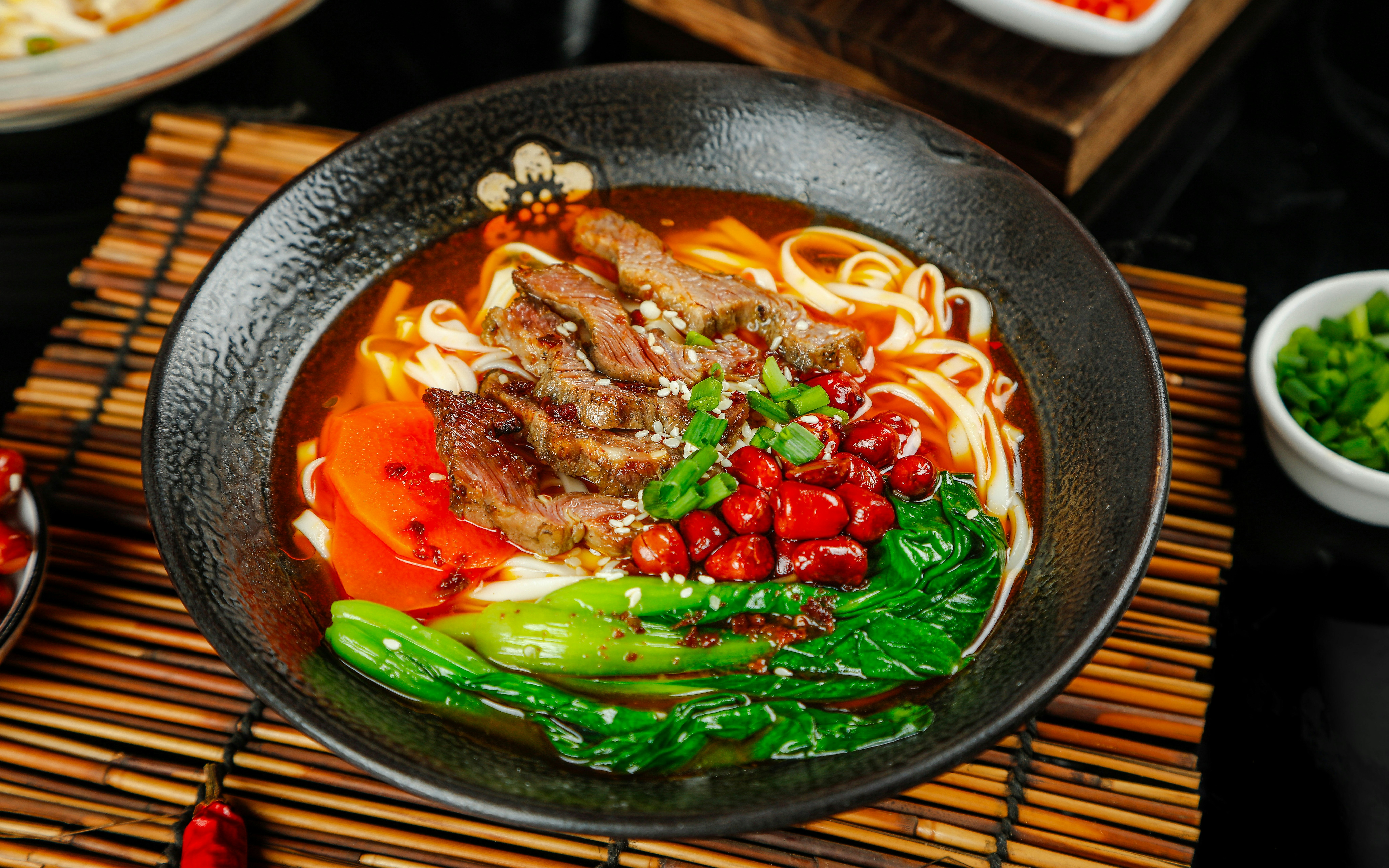 Asian beef noodle soup with vegetables in black bowl, featuring ramen noodles, beef slices, and greens.