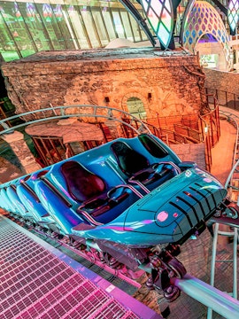 Roller coaster at Doha Quest Theme Park with vibrant lights and stone backdrop.