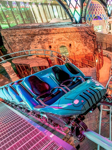 Roller coaster at Doha Quest Theme Park with vibrant lights and stone backdrop.