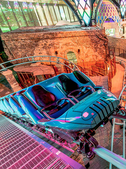 Roller coaster at Doha Quest Theme Park with vibrant lights and stone backdrop.