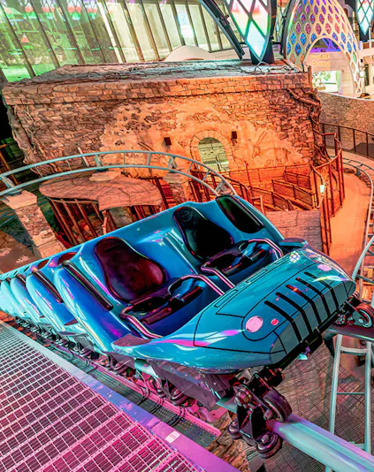 Roller coaster at Doha Quest Theme Park with vibrant lights and stone backdrop.