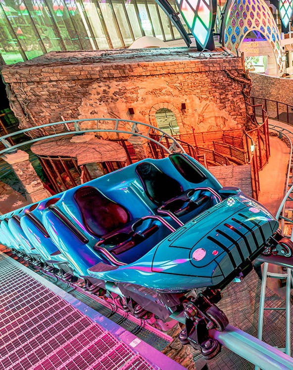 Roller coaster at Doha Quest Theme Park with vibrant lights and stone backdrop.