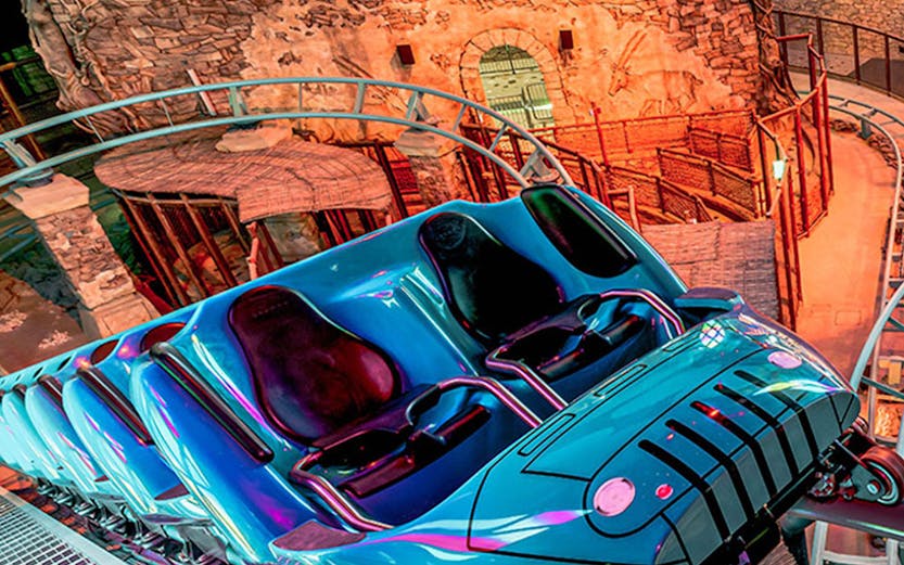 Roller coaster at Doha Quest Theme Park with vibrant lights and stone backdrop.