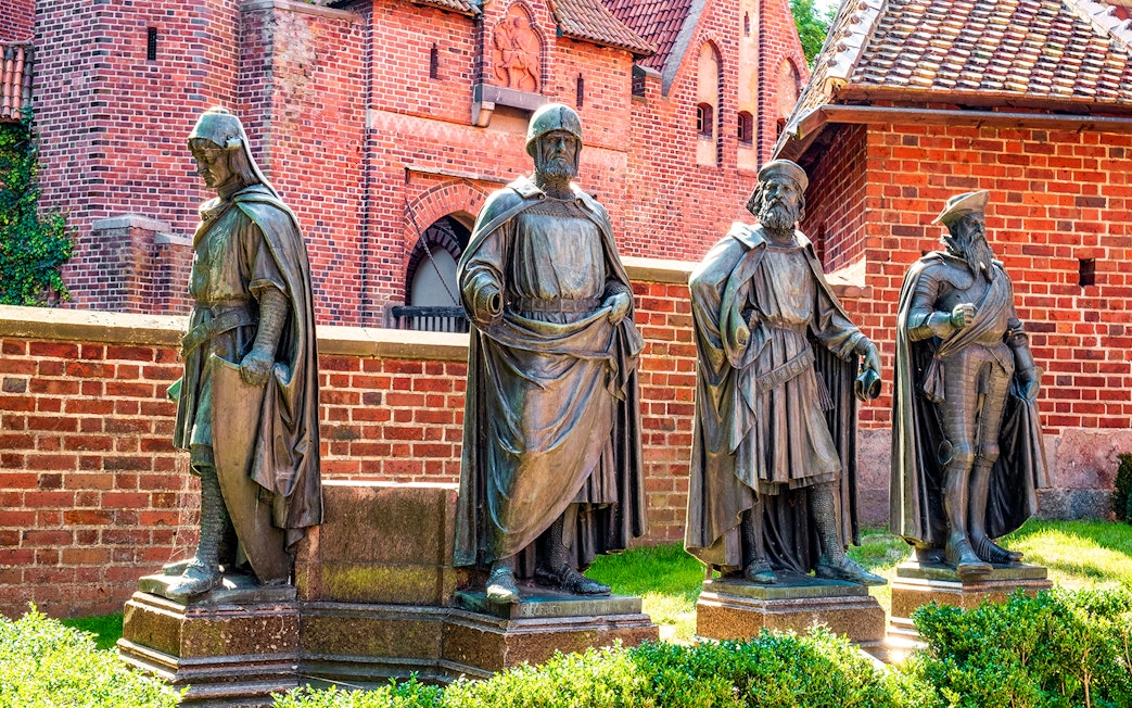 Statues of knights in front of Malbork Castle's red brick walls, Poland.
