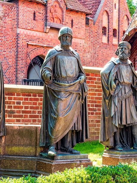 Statues of knights in front of Malbork Castle's red brick walls, Poland.